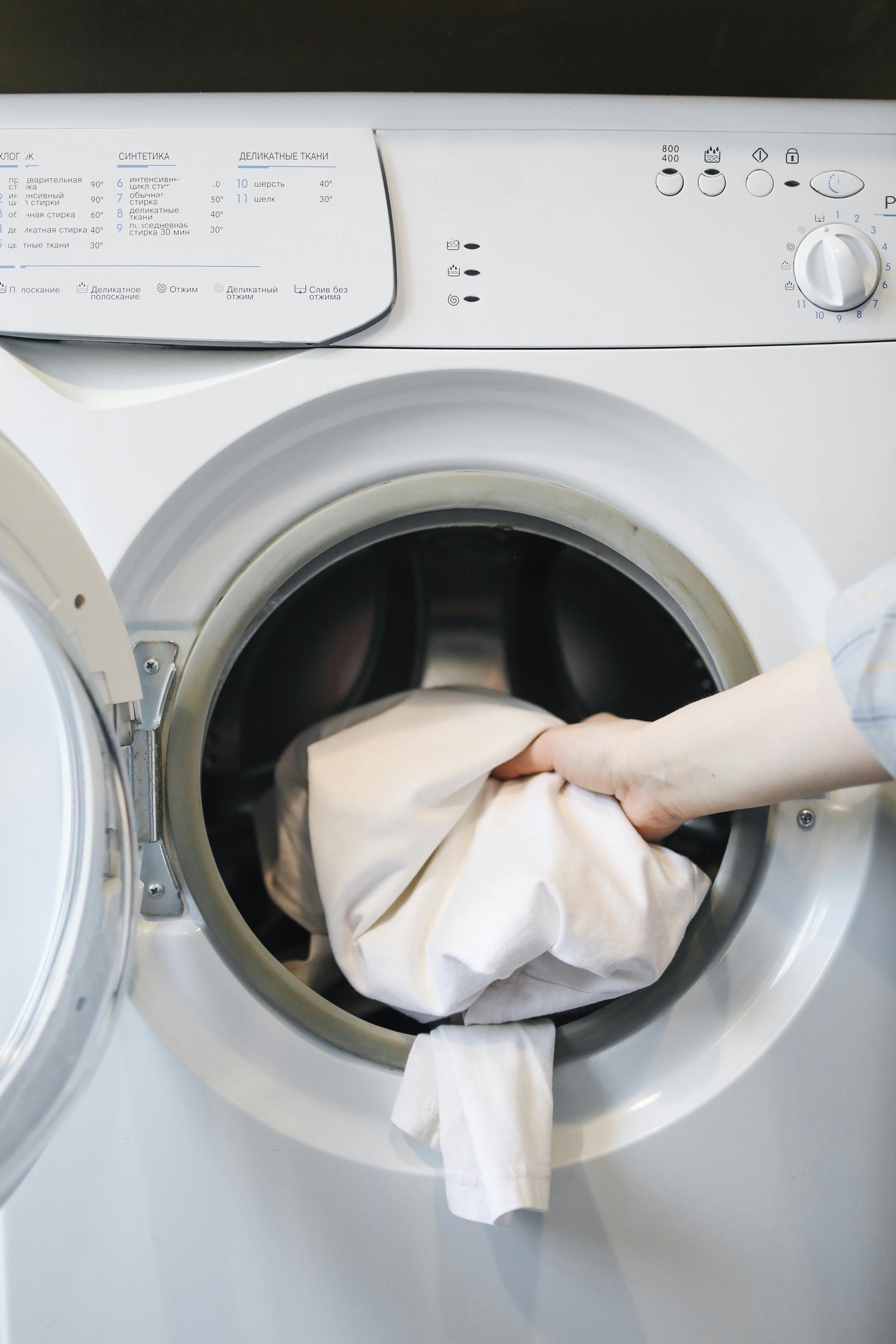 Person loading a white garment into an open washing machine.